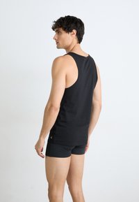 Schwarzes Tanktop aus Baumwolle mit Racerback-Design. Kombiniert mit schwarzen, engen Shorts, die einen schlichten und sauberen Look betonen.