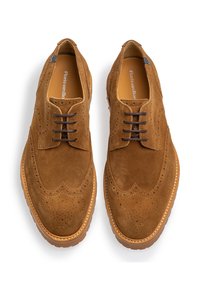 Zapatos de ante marrón con cordones y detalles de brogue, que cuentan con una puntera redonda, un upper texturizado y una suela de goma con una costura visible.