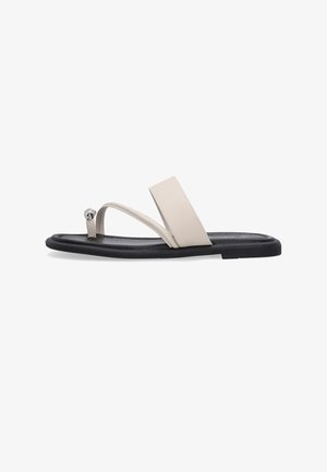 Flad sandal med sort sål, beige bred rem over midten og tynd tå-loop med sølvmetalisk detaljer.
