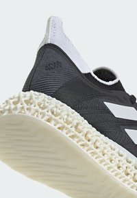 Black sneaker with a textured fabric upper, white accents, and a distinctive cream-colored, lattice-style midsole.