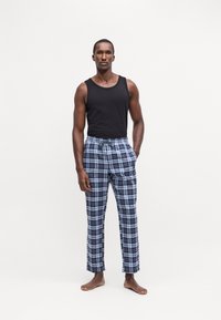 Crni top bez rukava uparen s plavim i sivim kariranim pidžama hlačama s podesivim strukom i džepovima, nošene na bosu nogu.