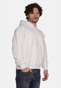 Felpa bianca con cappuccio, tasca frontale e laccetti, caratterizzata da una vestibilità comoda e polsini a costine, abbinata a jeans in denim blu.