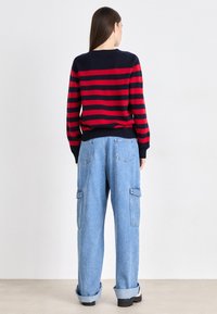 Pulover în dungi, navy și roșu, cu o margine ribbed, asociat cu pantaloni cargo lejeri, de culoare bleu deschis, care au buzunare laterale și manșete răsucite.