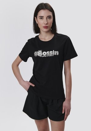 T-shirt noir en coton avec un texte en métal argenté "#Bossin" et "Je vais y arriver." Manches courtes, encolure ronde, coupe décontractée.