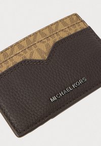 Brun læder kortholder med en tekstureret overflade, der har et lysebrunt mønster øverst, og sølv "MICHAEL KORS" branding foran.