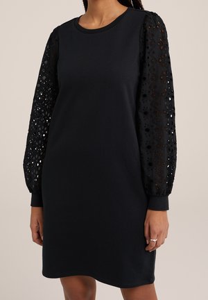 Sort kjole med rund halsudskæring og lange pufærmer i blonder med blomsterudskæringsmønstre.