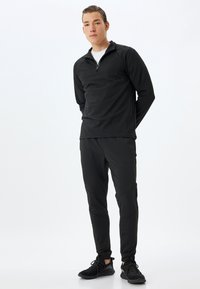 Conjunto atlético negro que incluye una parte superior de manga larga con cremallera y pantalones ajustados. Fabricado con un material suave y elástico, con un sutil detalle de costura.