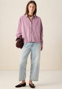 Light purple button-up shirt, relaxed fit, paired with light blue wide-leg jeans and dark brown flat shoes with studs. Brown patterned handbag.