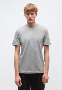 Szürke rövid ujjú póló kerek nyakkivágással, ellentétes színű csíkos szegéllyel az ujjakon. Puha, könnyű anyag a kényelemért.