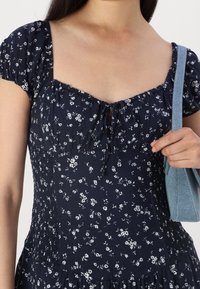 Námo�řnické květinové šaty s krátkými nabíranými rukávy, čtvercovým výstřihem a šňůrkou v oblasti hrudníku. Mají na bocích elastické nařasení a splývavou sukni.