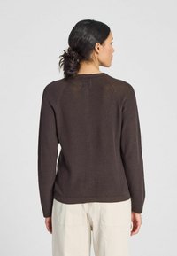 Brauner gestrickter Pullover mit Rundhalsausschnitt, gerippten Bündchen und Saum. Hat Raglanärmel und eine glatte Textur mit dezenten Nähdetails.