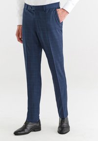 Granatowe spodnie w kratę o dopasowanym kroju, z płaskim przodem i szlufkami na pasek, w połączeniu z błyszczącymi czarnymi butami eleganckimi.