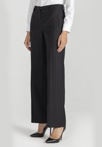 Czarne spodnie w prążki o szerokim fasonie, z przednimi kieszeniami i dopasowanym pasem, w zestawieniu z czarnymi szpilkami na spiczastym nosku.