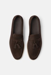 Mocassins en daim marron avec des détails à pampilles, bout rond, semelle contrastante et accents cousus. Texture lisse et design à enfiler.