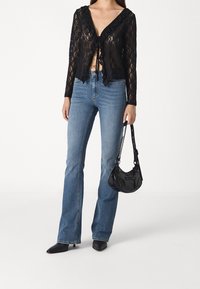 Top de encaje negro con escote con volantes, atado en la parte delantera; combinado con jeans de campana azul claro y un pequeño bolso negro. Tacones negros de punta.