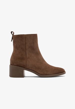 Brązowe zamszowe botki za kostkę z okrągłym noskiem, słupkowym obcasem i pętlą do zakupu z tyłu. Charakteryzują się minimalnymi detalami szwów wzdłuż podeszwy.