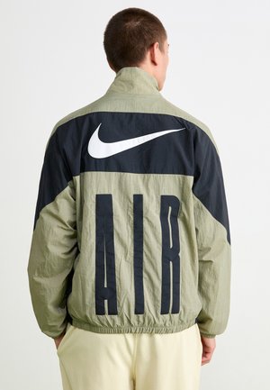 Nike striukė, pasižyminti lengvu, raukšlėtu audiniu, juoda viršutine dalimi, dideliu juodu "AIR" užrašu ir ryškia balta logo.