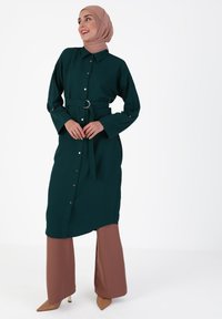 Turquoise long button-down dress with a tie belt, featuring a collar, long sleeves, and a slightly flared hem, paired with brown wide-leg pants.