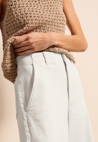 Top de tirantes de ganchillo beige combinado con pantalones de algodón blancos de tiro alto, que cuentan con bolsillos frontales y un corte relajado.