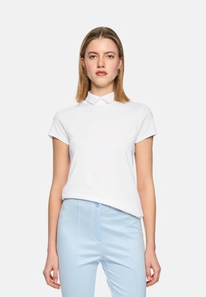 White short-sleeve polo shirt with a pointed collar, made of smooth fabric. Paired with light blue tailored pants, featuring a button closure.
