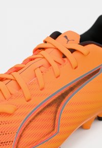 Ποδοσφαιρικά παπούτσια Puma με φωτεινό πορτοκαλί συνθετικό πάνω μέρος, μαύρη επένδυση, έντονες γκρίζες λεπτομέρειες και υφή στον σχεδιασμό, καθώς και σύστημα κορδονιών.