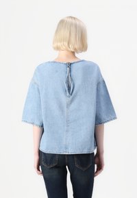Top in denim blueto, morbido e leggermente oversize, con maniche corte e scollo rotondo. Presenta una chiusura a cerniera al centro sul retro, cuciture a vista e una texture morbida.