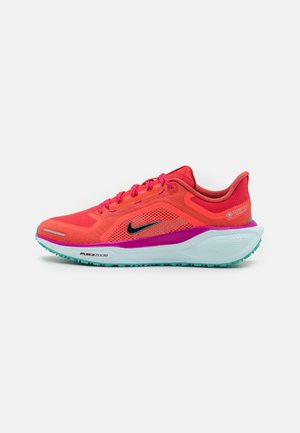 Chaussure de course Nike corail vif avec lacets roses, swoosh noir, accent violet sur la semelle intermédiaire, semelle blanche amortie à l'air et semelle extérieure turquoise.