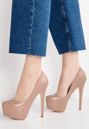 Chaussures à plateforme à talons hauts nudes avec une finition brillante, bout effilé et talon aiguille fin, associées à un pantalon en denim court.