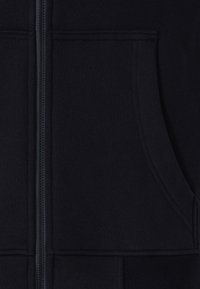 Navy Zip-Hoodie aus weichem Stoff, mit einem vorderen Reißverschluss, Seitentaschen, gerippten Bündchen und einer sauberen, glatten Textur.