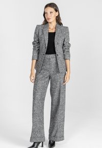 Dopasowana szara marynarka z poduszkami na ramionach, zestawiona z wysokim stanem szerokimi spodniami, obie z teksturowanej tkaniny. Czarny top pod spodem.