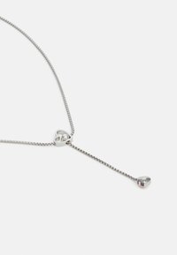 Zilveren ketting met een hartvormige hanger die een heldere edelsteen bevat en een taps toelopend uiteinde heeft. Soepele textuur met een eenvoudig, minimalistisch ontwerp.