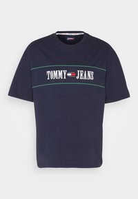 Maglietta in cotone blu navy con maniche corte, caratterizzata da un logo bianco "TOMMY JEANS" e una linea di accento verde che attraversa il petto.
