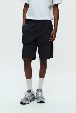 Shorts navy, confecționați dintr-un material ușor, cu o talie elastică și buzunare laterale. Asortați cu adidași gri și șosete albe.