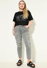 Camiseta negra con dibujo abstracto de líneas blancas; jeans ajustados en gris claro desgastados con rotos; sandalias negras de plataforma; corte recto.