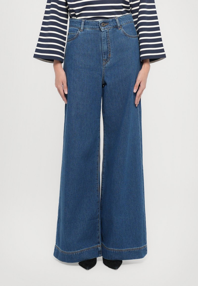 Jeans a vita alta e gamba larga in denim blu medio. Presentano una chiusura con bottone e cerniera, con cuciture a contrasto e tocchi di orlo sfrangiato.