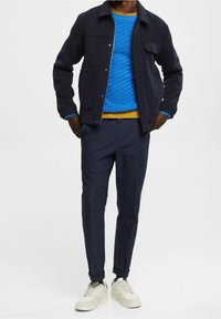 Námořnický vlněný kabát, modrý texturovaný svetr, žlutý pas, námořnické chinos kalhoty a bílé tenisky. Jednoduchý design s kontrastními barvami.