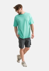 T-shirt vert menthe à manches courtes en coton, associé à un short cargo gris avec poches et manches retroussées ; porté avec des baskets grises.