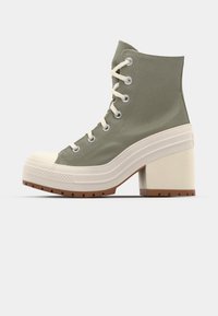 Zapatillas deportivas de plataforma altas verdes con parte superior de lona, puntera de goma color crema y tacón grueso. Presenta ojales de metal y diseño con cordones.