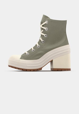 Sapatilhas de plataforma altas verdes com parte superior em lona, biqueira de borracha creme e salto robusto. Apresentam ilhós de metal e design de atacadores.