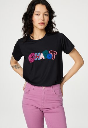 Schwarzes T-Shirt mit buntem gesticktem Text "CHAPOT". Kombiniert mit pinken Jeans, die einen glatten Stoff und eine taillierte Passform zeigen.