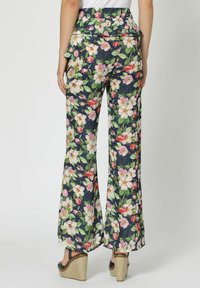 Mujer que viste pantalones anchos de flores en azul marino y sandalias de cuña negras, mostrada desde atrás con una blusa blanca visible en la cintura.