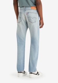 Ljust blå denimjeans med rak passform, med två bakfickor och en brun läderlapp på midjebandet.