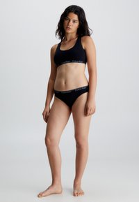 Svart bomullsbralette og bikiniset med en tykk elastisk linning med "Calvin Klein"-logo. Enkelt design, sømløse kanter, tettsittende form.