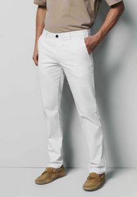Witte katoenen broeken met een rechte pasvorm, voorzien van een knoopsluiting aan de voorkant en zijzakken, gecombineerd met lichtbruine moccasin-stijl schoenen.