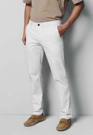 White cotton trousers with a straight fit, featuring a front button closure and side pockets, paired with light brown moccasin-style shoes.