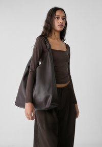 Brown leather hobo bag with a soft texture, rounded shape, and a knotted handle detail, carried over the shoulder against a light background.