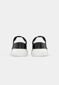 Zwarte sneakers met een gladde afwerking, witte accent op de hiel en een gestructureerde rubberen zool. Bevat branding op de achterkant.