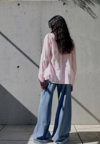 Jeans in denim chiaro a taglio comodo abbinati a una maglietta a maniche lunghe rosa e bianca a righe. Sullo sfondo si vede un muro di cemento.