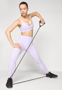 Light purple sports bra and matching high-waisted leggings, with a fitness resistance band in black, positioned diagonally on the floor.