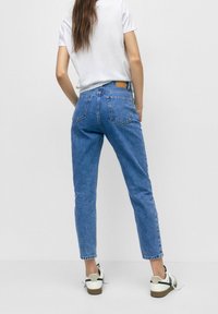 Jean en denim bleu taille haute avec une coupe droite, comprenant deux poches arrière et une étiquette en cuir marron à la taille.